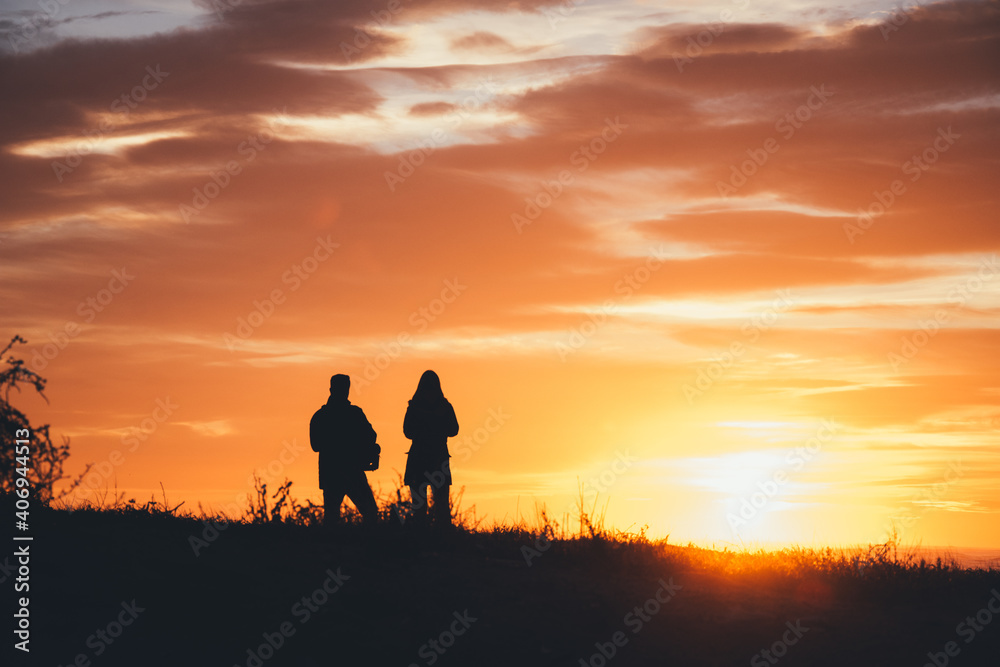 Silueta de pareja delante del mar mirando al sol durante el atardecer