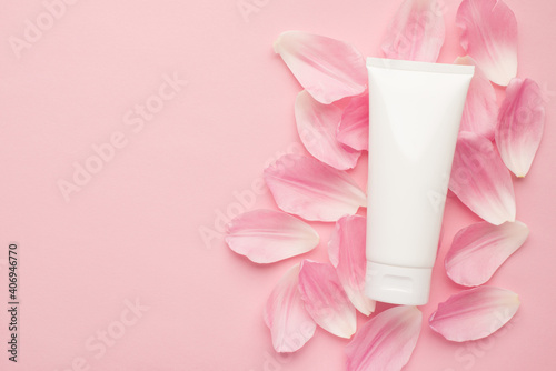 Flat lay top view photo of white cream bottle lying in flower petals isolated pastel color backdrop with empty blank space