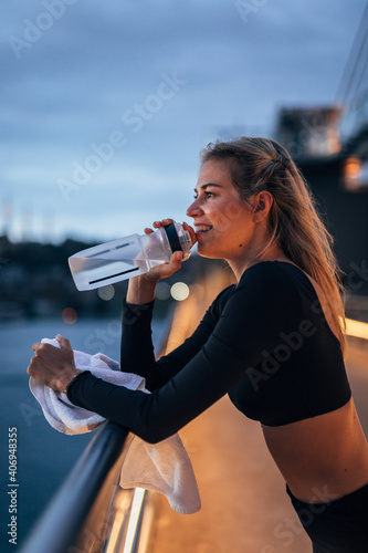 young woman holding her water bottle and smiling after doing her outdoor morning workout 