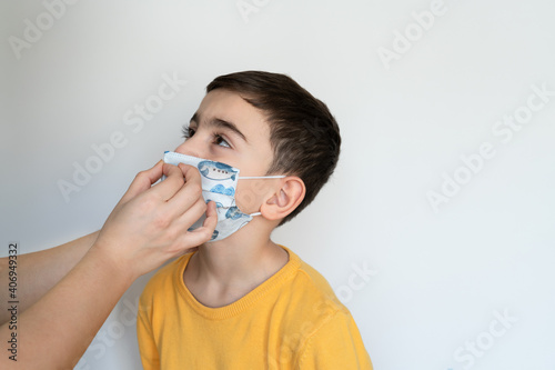 mother wears a mask on her son. woman helps to child. boy wears colorful protective medical face mask isolated white background portrait photo. during coronavirus outbreak. 2021 pandemic lockdown.