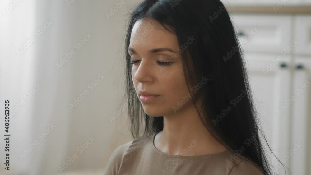 A young slender and pretty brunette woman in sportswear sits and meditates with her eyes closed in a home interior. Meditation at home, calm after a working day. Close-up of the head. 4K 50fps