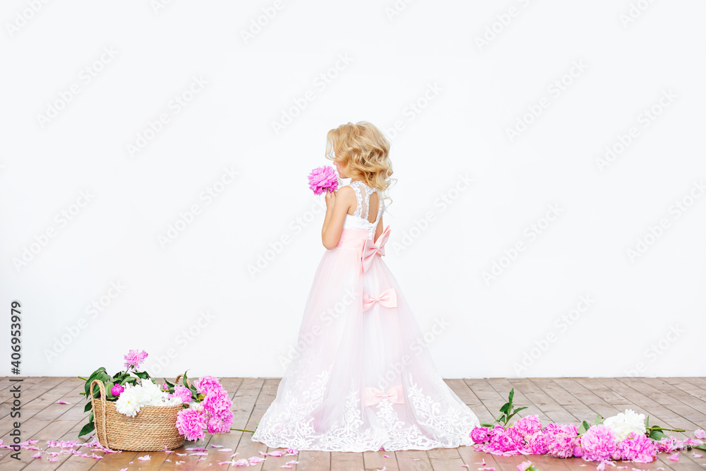 Little beautiful child girl in luxury dress with peonies in indoor white background