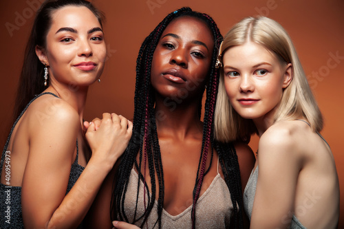 young pretty caucasian, afro, asian woman posing cheerful together on brown background, lifestyle diverse nationality people concept