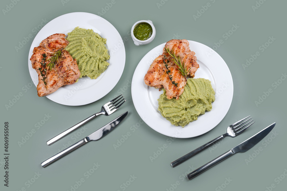 Delicious grilled chicken with herbs and green puree. Chicken fillet with mashed potatoes, green peas and pesto sauce. Healthy homemade food. Flat lay, top view. Delicious grilled chicken with herbs and green puree. Chicken fillet with mashed potatoes, green peas and pesto sauce. Healthy homemade food. Flat lay, top view.