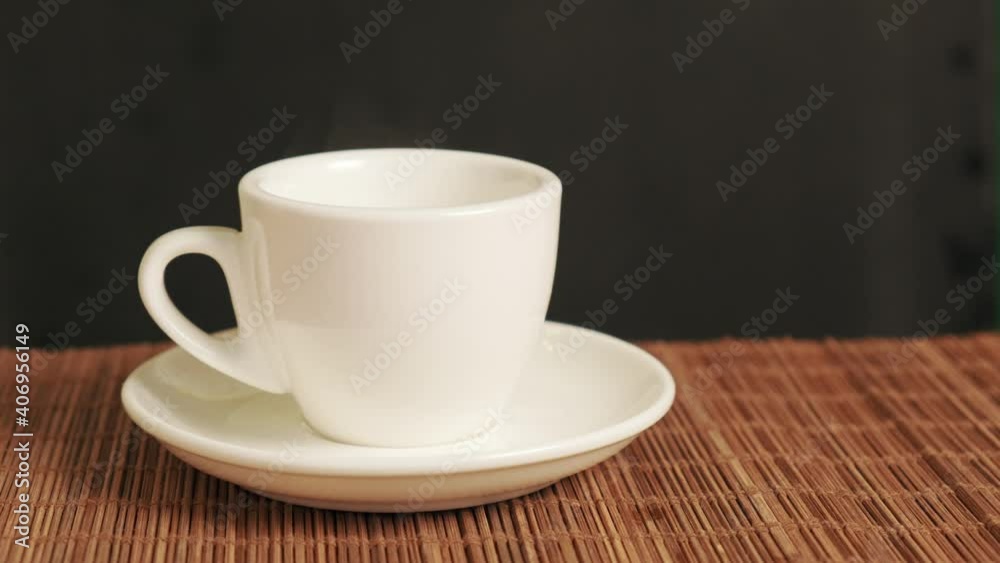 A woman puts a white fragrant coffee cup on the table. There is a bamboo mat on the table. A woman puts a white fragrant coffee cup on the table. There is a bamboo mat on the table.