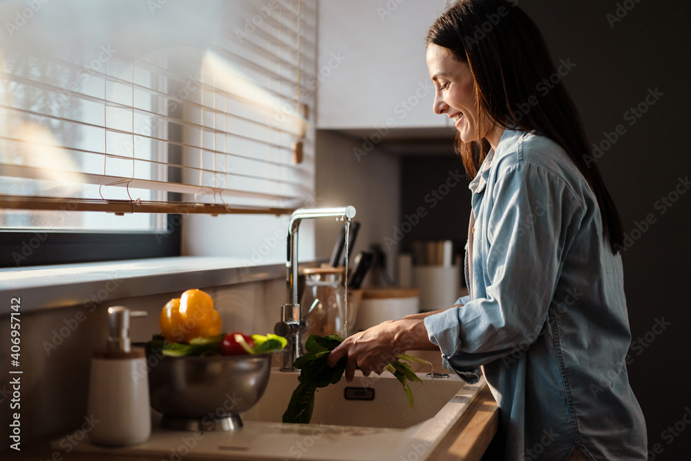 Smiling young woman washing vegetable in the sink Smiling young woman washing vegetable in the sink