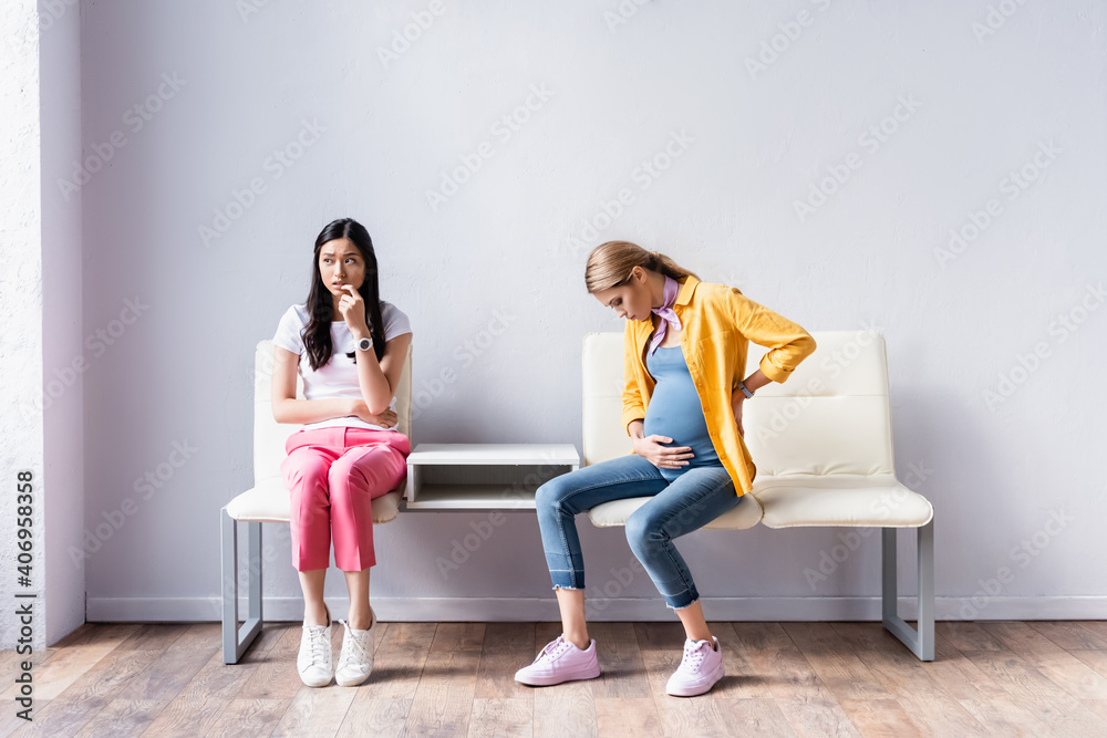 Obraz premium Pregnant woman sitting near worried asian woman in queue