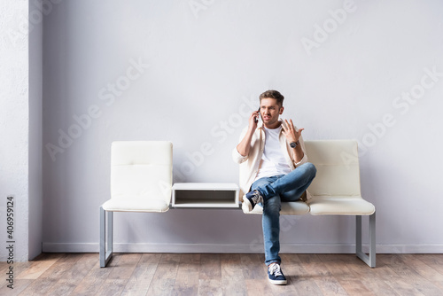 Angry man talking on smartphone while waiting in hall