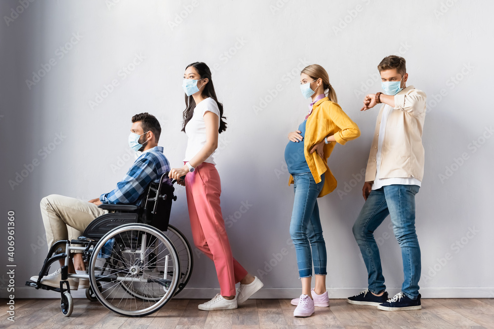 Multiethnic people in medical mask standing near disabled man and pregnant woman in hall Multiethnic people in medical mask standing near disabled man and pregnant woman in hall