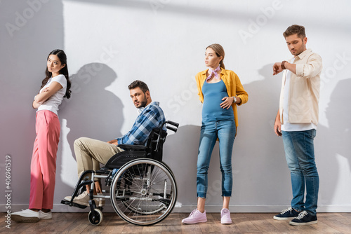 Multiethnic people and disabled man standing near wall in queue