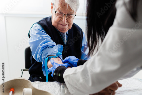 Nurse drawing blood from an elderly man in his home. Home care.