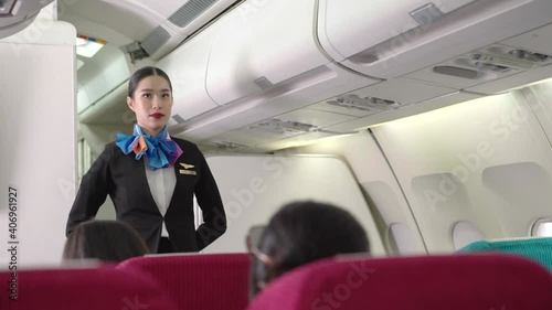 Asian female air hostess standing in  front of cabin seat, watching and checking passenger ready on airplane before takeoff. safety and business security. travel or go to work abroad concept