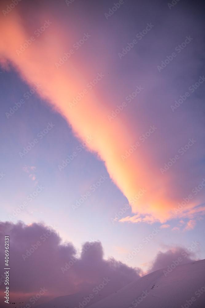 Fototapeta premium Sunset detail on the plain of castelluccio di norcia, in italy. The plain is covered with snow. The warm sunset hits the clouds illuminating them with colors: pink, yellow, red.