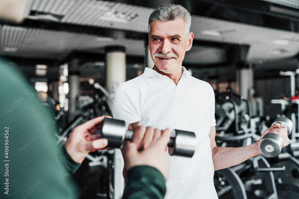 Portrait of a mature man performing an exercise with dumbbells, a rehabilitation coach helps him