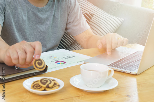 Man working at home with laptop on the table and enjoy with cookies.