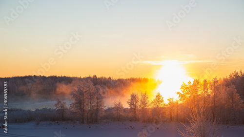 Fabulous winter landscape with fog illuminated by the orange light of the winter sun in frosty weather in the forest