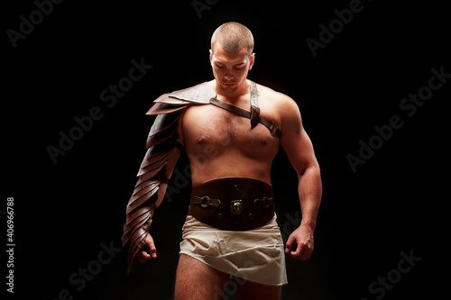 Gladiator with sword and armor on a black background. A warrior in gladiatorial armor looks dawn at a beam of light
