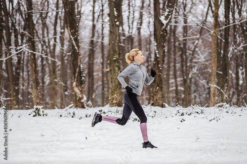 Fast slim sportswoman running in forest at snowy winter day. Race, jogging in nature, winter fitness