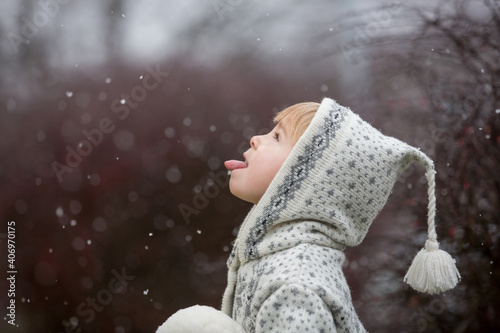 Beautiful blond toddler child, boy, with handmade knitted sweater playing in the park with first snow photo
