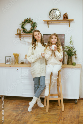girls in warm light knitted sweaters in the kitchen with cups of warm cocoa