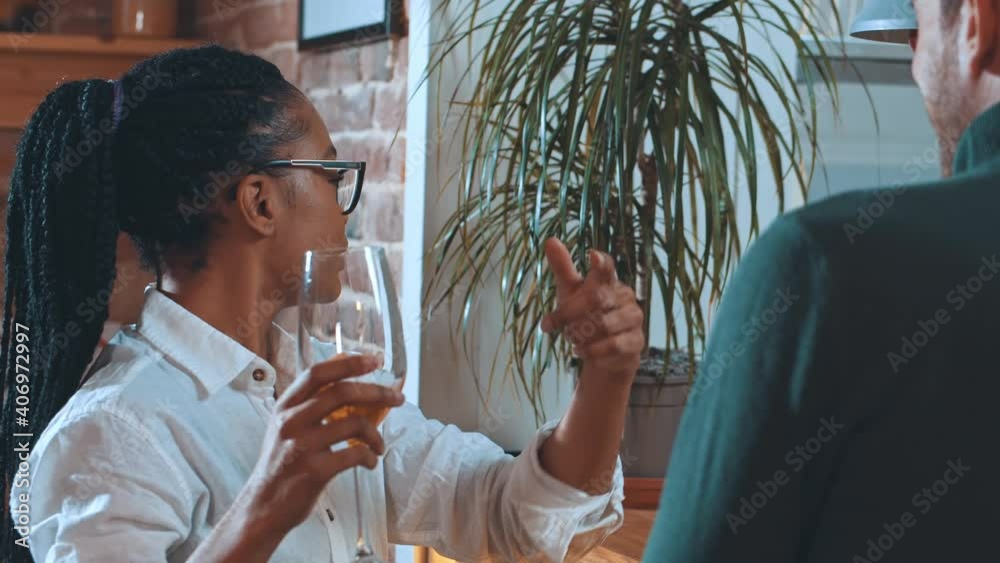 Young funny afro-american drunk woman drinking wine in glass while dating with her boyfriend standing at bartender together.