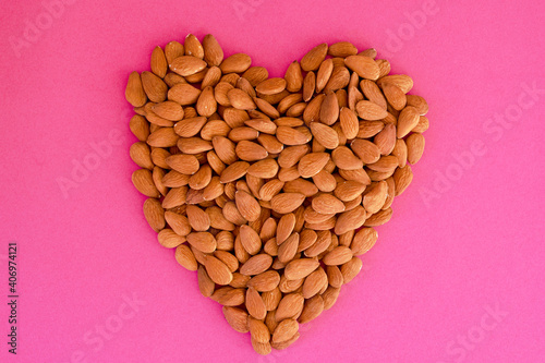 Almonds heap in heart shape on pink background. Isolated. Valentine's Day. Flat lay. Top view. Raw food.