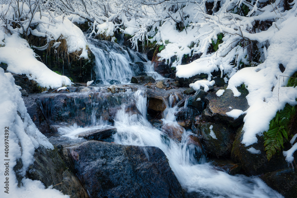Small stream among wet stones and white snow in the picturesque Carpathian mountains in Ukraine Small stream among wet stones and white snow in the picturesque Carpathian mountains in Ukraine