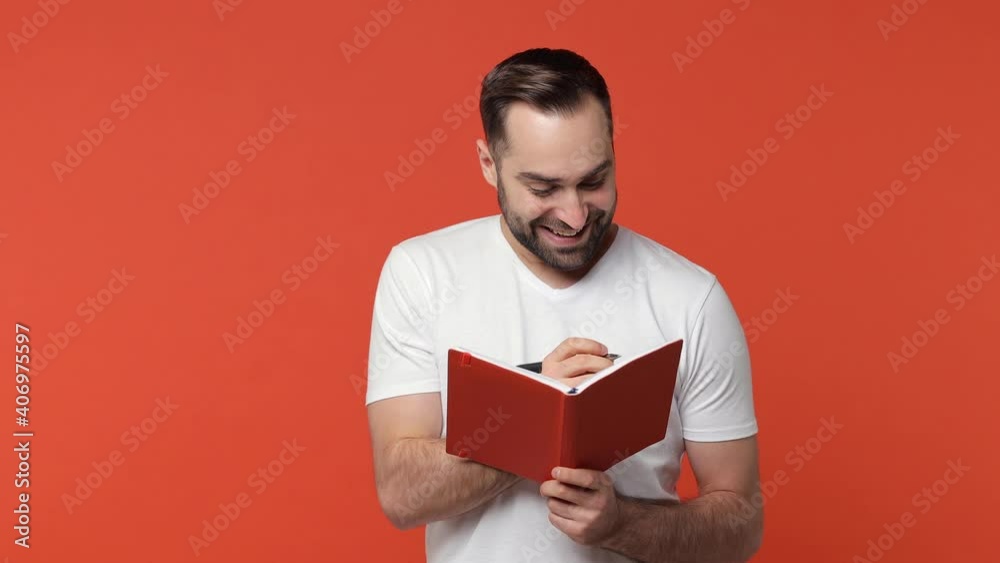 Pensive excited bearded young man 20s in white casual t-shirt isolated on orange color wall background studio. People lifestyle concept. Holding pen up with great new idea writing notes in notebook Pensive excited bearded young man 20s in white casual t-shirt isolated on orange color wall background studio. People lifestyle concept. Holding pen up with great new idea writing notes in notebook