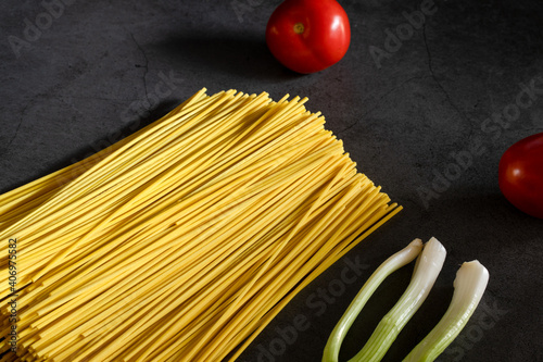 Yellow spaghetti and tomatoes on a black marble table. Yellow Italian Pasta. Raw spaghetti. Italian concept and menu