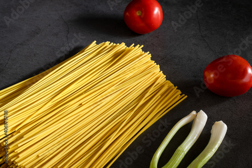 Yellow spaghetti and tomatoes on a black marble table. Yellow Italian Pasta. Raw spaghetti. Italian concept and menu