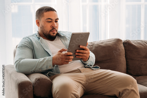 Young man using digital tablet surfing the internet on the couch in the living room 
