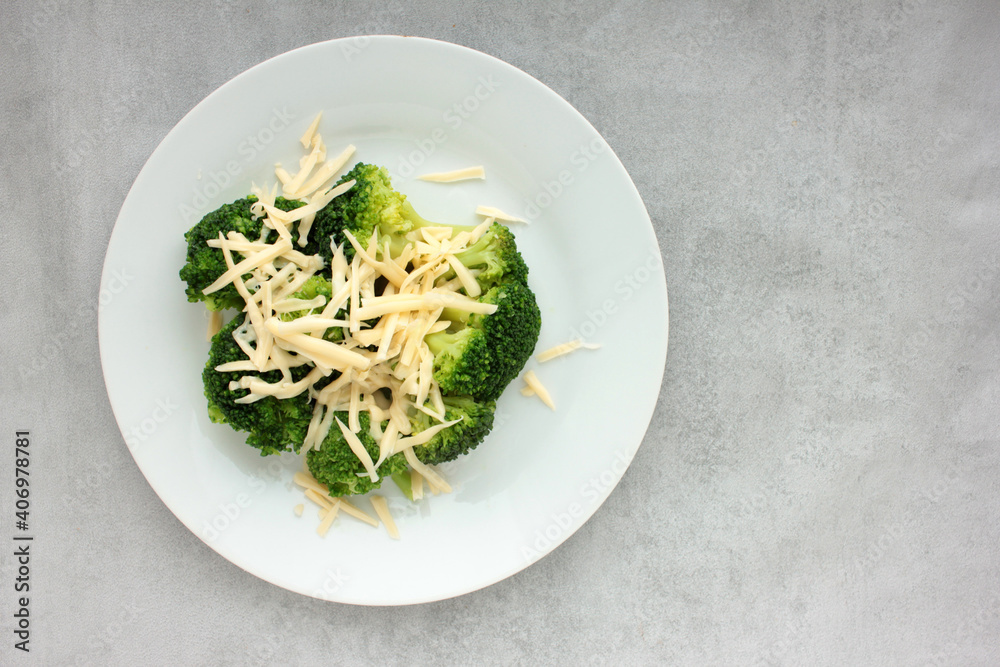 Broccoli with grated cheese on a plate on gray concrete background. Healthy food. Flat lay, close-up Broccoli with grated cheese on a plate on gray concrete background. Healthy food. Flat lay, close-up