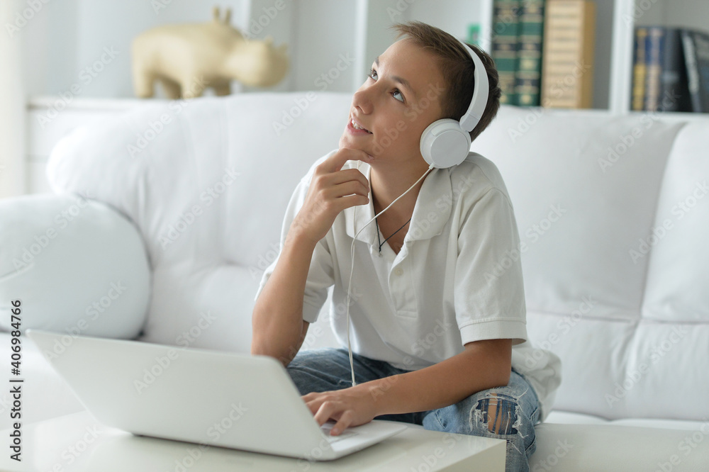 Cute boy in headphones using laptop in room Cute boy in headphones using laptop in room