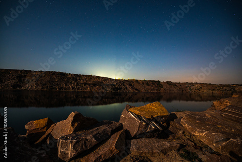Old flooded stone quarry surrounded by stone waste from a mine work against a beautiful night sky