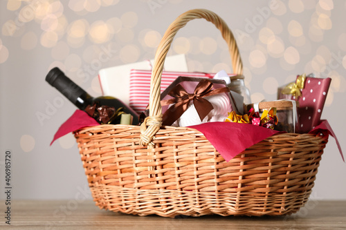 Wicker basket with gifts, wine and food against blurred festive lights. Space for text photo