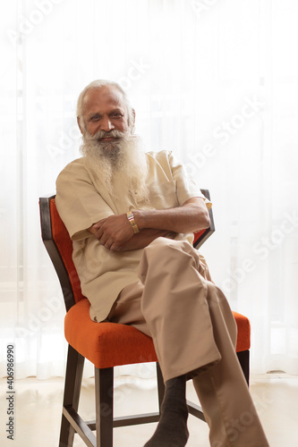 A CONFIDENT OLD MAN SITTING AND POSING IN FRONT OF CAMERA	 photo