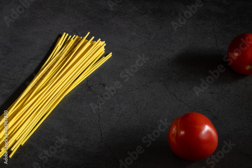 Yellow spaghetti and tomatoes on a black marble table. Yellow Italian Pasta. Raw spaghetti. Italian concept and menu