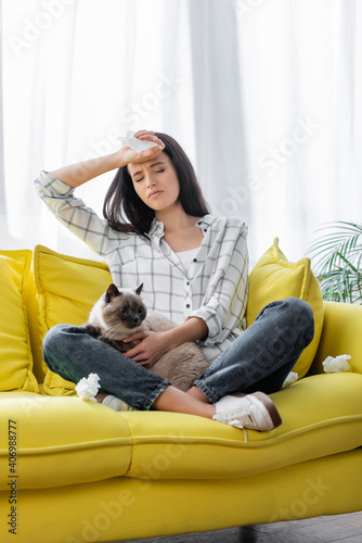 allergic woman suffering from headache while sitting on sofa with cat