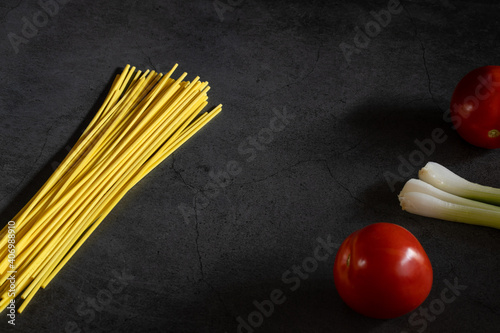 Yellow spaghetti and tomatoes on a black marble table. Yellow Italian Pasta. Raw spaghetti. Italian concept and menu