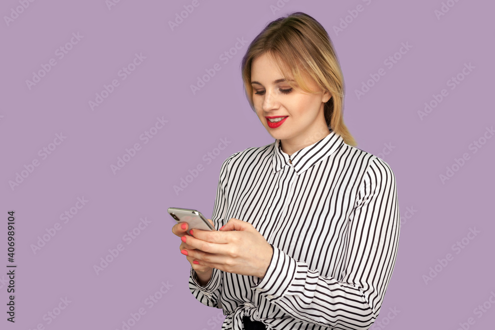 Portrait of happy beautiful businesslady with red lips in glamour striped blouse using cellphone, smiling, typing message to partner on mobile phone. indoor studio shot isolated on purple background Portrait of happy beautiful businesslady with red lips in glamour striped blouse using cellphone, smiling, typing message to partner on mobile phone. indoor studio shot isolated on purple background