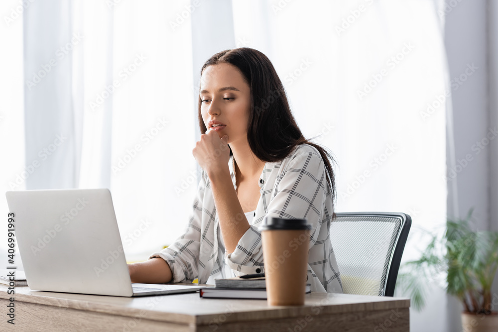 thoughtful freelancer working at laptop near coffee to go on blurred foreground thoughtful freelancer working at laptop near coffee to go on blurred foreground
