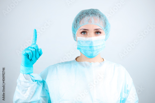 a nurse in a medical gown  mask and protective gloves shows an index finger up