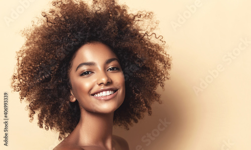Beauty portrait of african american woman with clean healthy skin on beige background. Smiling beautiful afro girl.Curly black hair. Black teen girl