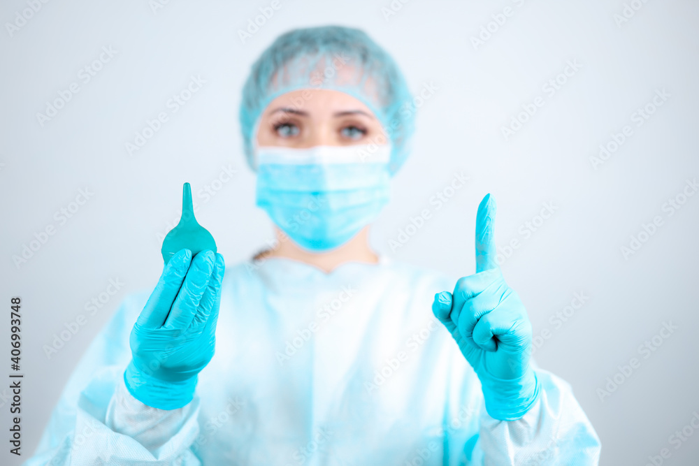 A nurse in a medical gown, mask and protective gloves holds an enema in her hands A nurse in a medical gown, mask and protective gloves holds an enema in her hands
