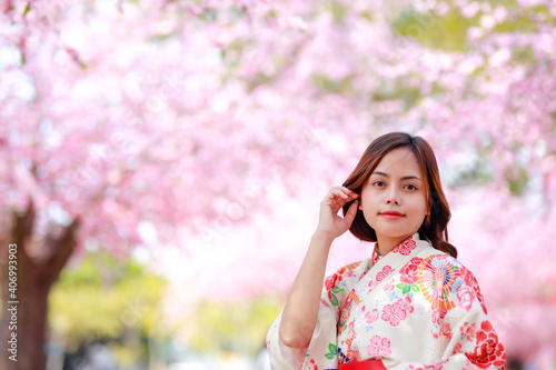 Portrait of a traveler young asian woman wear a dress yukata and walking on tree path in japan cherry blossoming sakura park at sunlight afternoon.