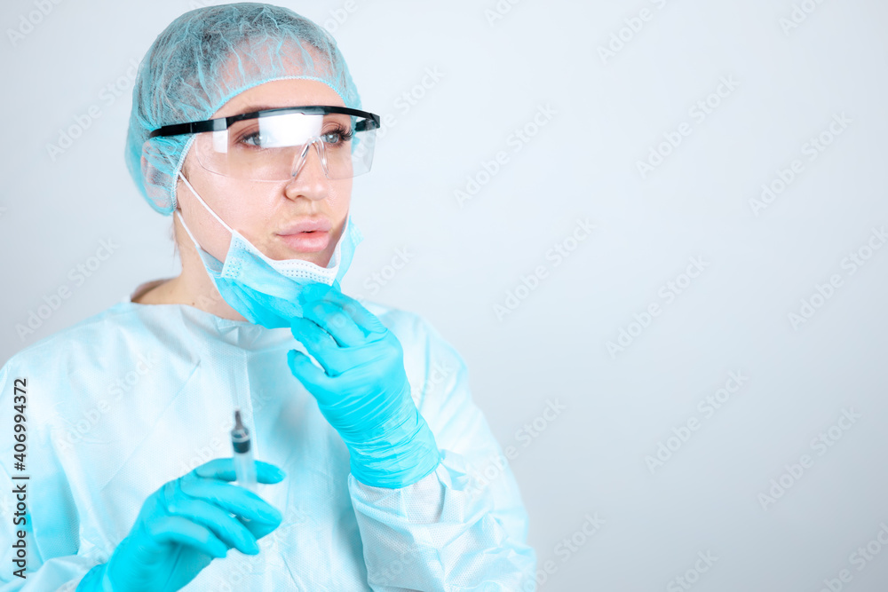A nurse in a medical gown, mask and protective gloves with transparent glasses removes the mask from her face A nurse in a medical gown, mask and protective gloves with transparent glasses removes the mask from her face