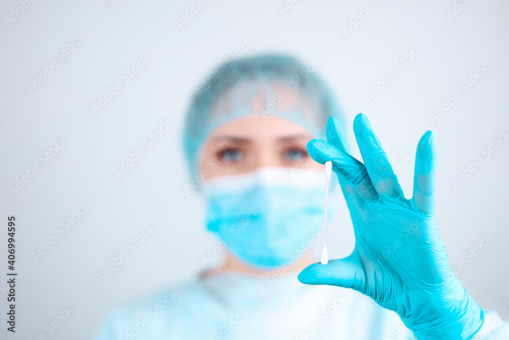 A nurse in a medical gown, mask and protective gloves holds a cosmetic cotton swab A nurse in a medical gown, mask and protective gloves holds a cosmetic cotton swab