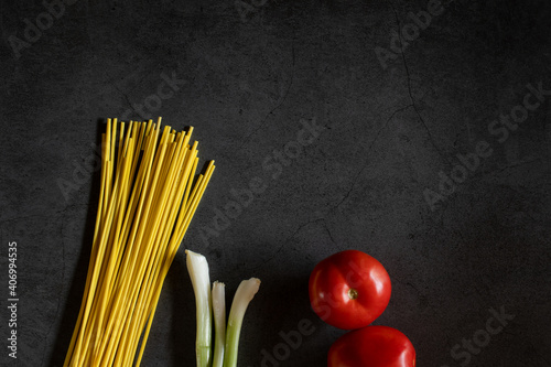 Yellow spaghetti and tomatoes on a black marble table. Yellow Italian Pasta. Raw spaghetti. Italian concept and menu