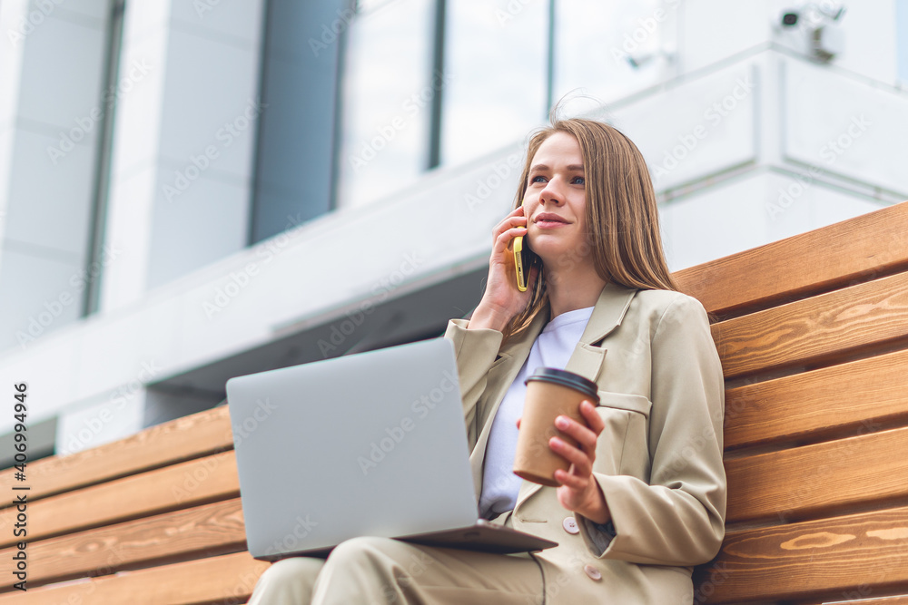Beautiful business woman talking over the phone and working in laptop sit down on bench outdoors. Happy student lady girl distance learning and online education. Beautiful business woman talking over the phone and working in laptop sit down on bench outdoors. Happy student lady girl distance learning and online education.