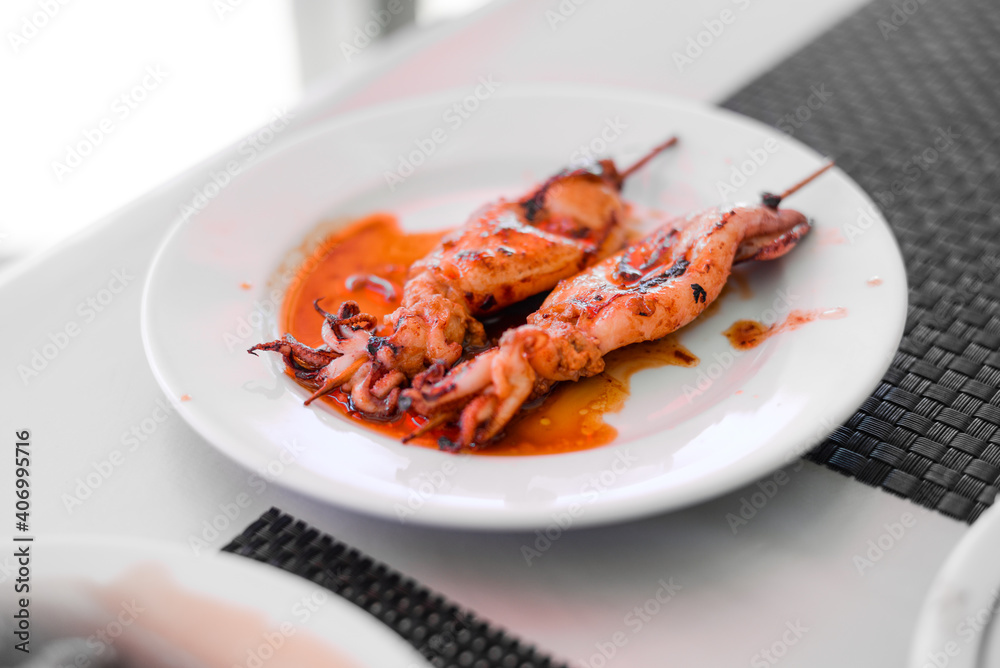 Grilled Squids on wooden sticks on white plate in spicy sause. A dish of Chinese cuisine. Grilled Squids on wooden sticks on white plate in spicy sause. A dish of Chinese cuisine.